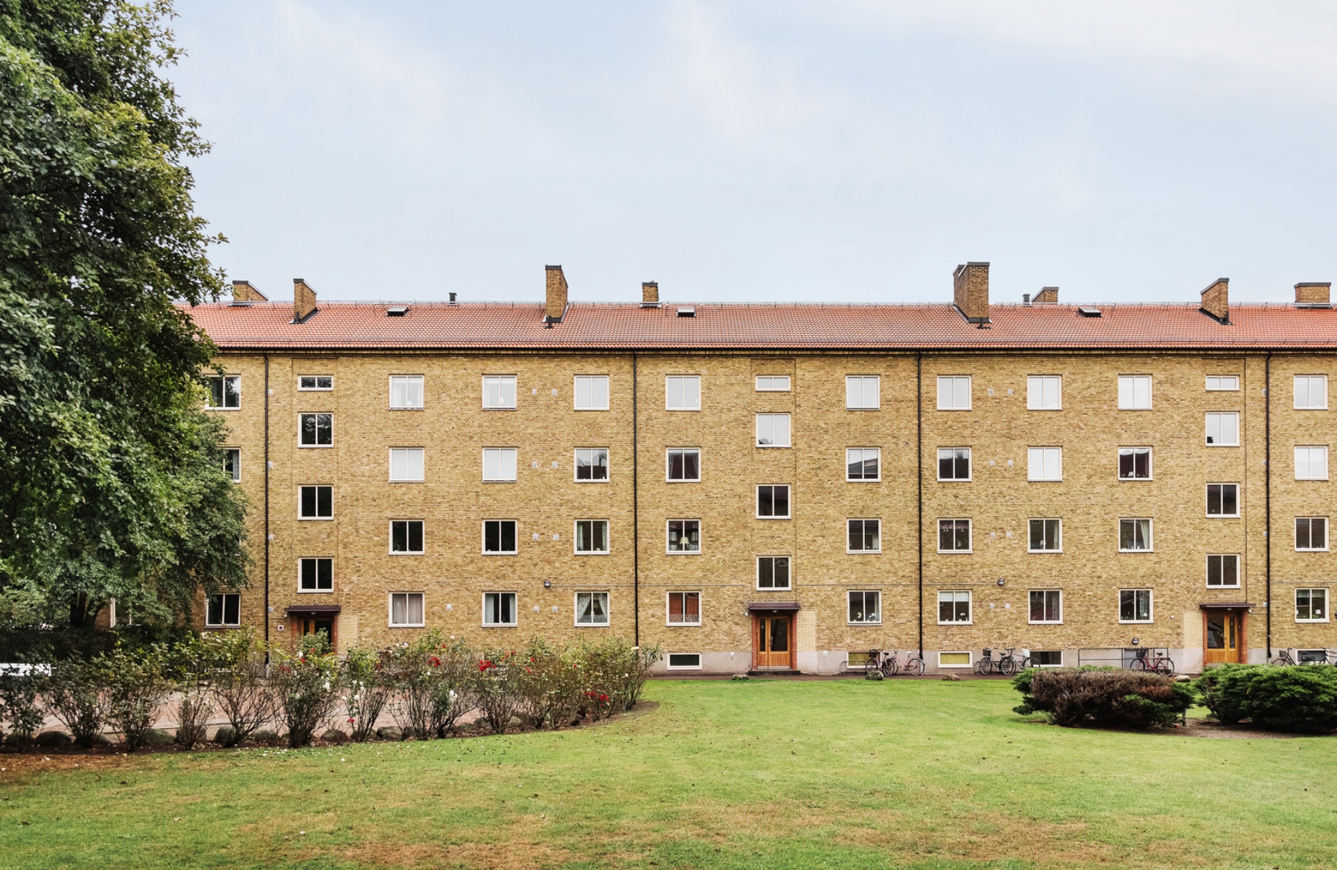 exteriör bild av klarabos fastighet Navaren i helsingborg. en gulteglad bostadsfastighet med grönska i förgrunden