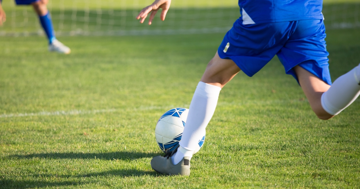 Fotbollsspelare i blå matchställ på gräsplan i färd med att sparka en boll – ett ögonblick från en fotbollsmatch eller träning.